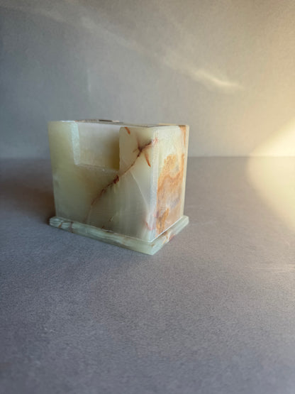 Square stone coaster holder in ivory and amber tones with natural rust lines, hand-carved from onyx.