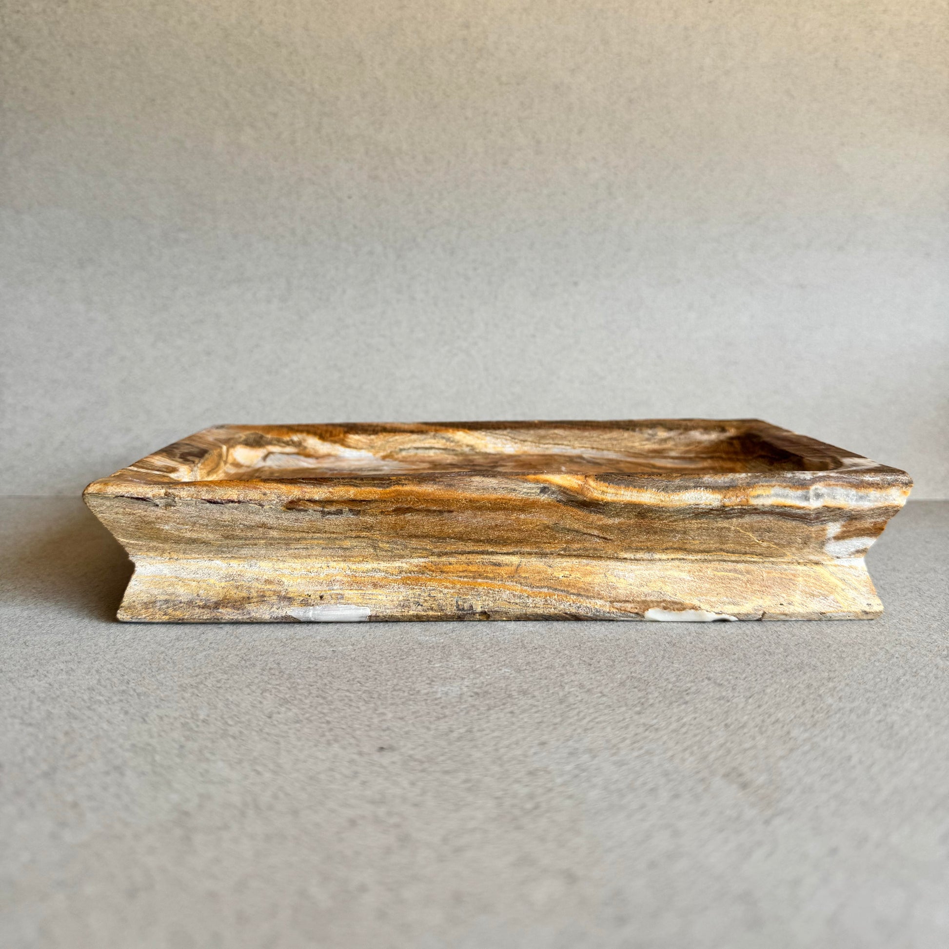 Hand-carved onyx catchall tray in rich amber and ivory tones on gray backdrop

