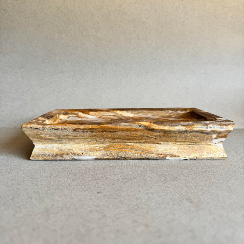 Hand-carved onyx catchall tray in rich amber and ivory tones on gray backdrop

