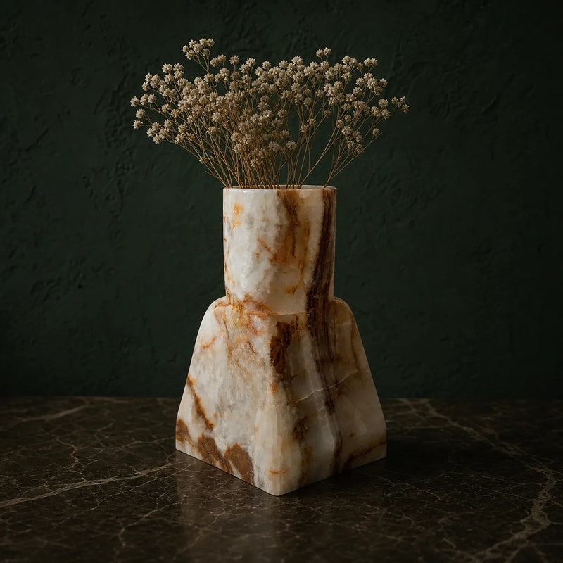 Hand-carved ivory onyx dune vase with a straight neck on a tapered base, webbed with rust and ember veining, holding dried baby's breath on a dark marble surface against a forest green wall