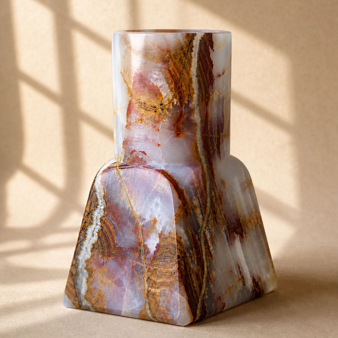 Close-up of a natural onyx vase showing amber and rust banded veining rising from a square base to a round neck
