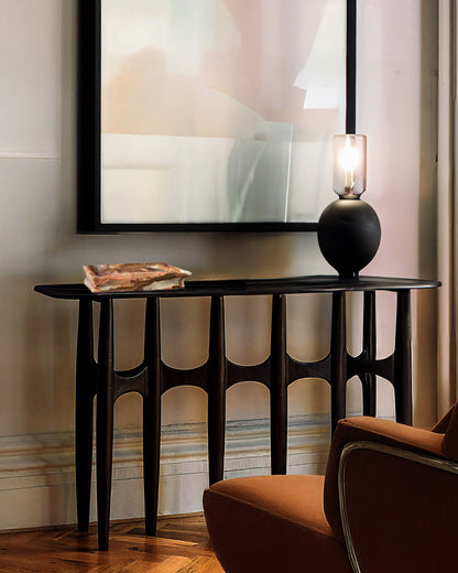 Black console table with a lamp and decorative item against a wall with abstract art.