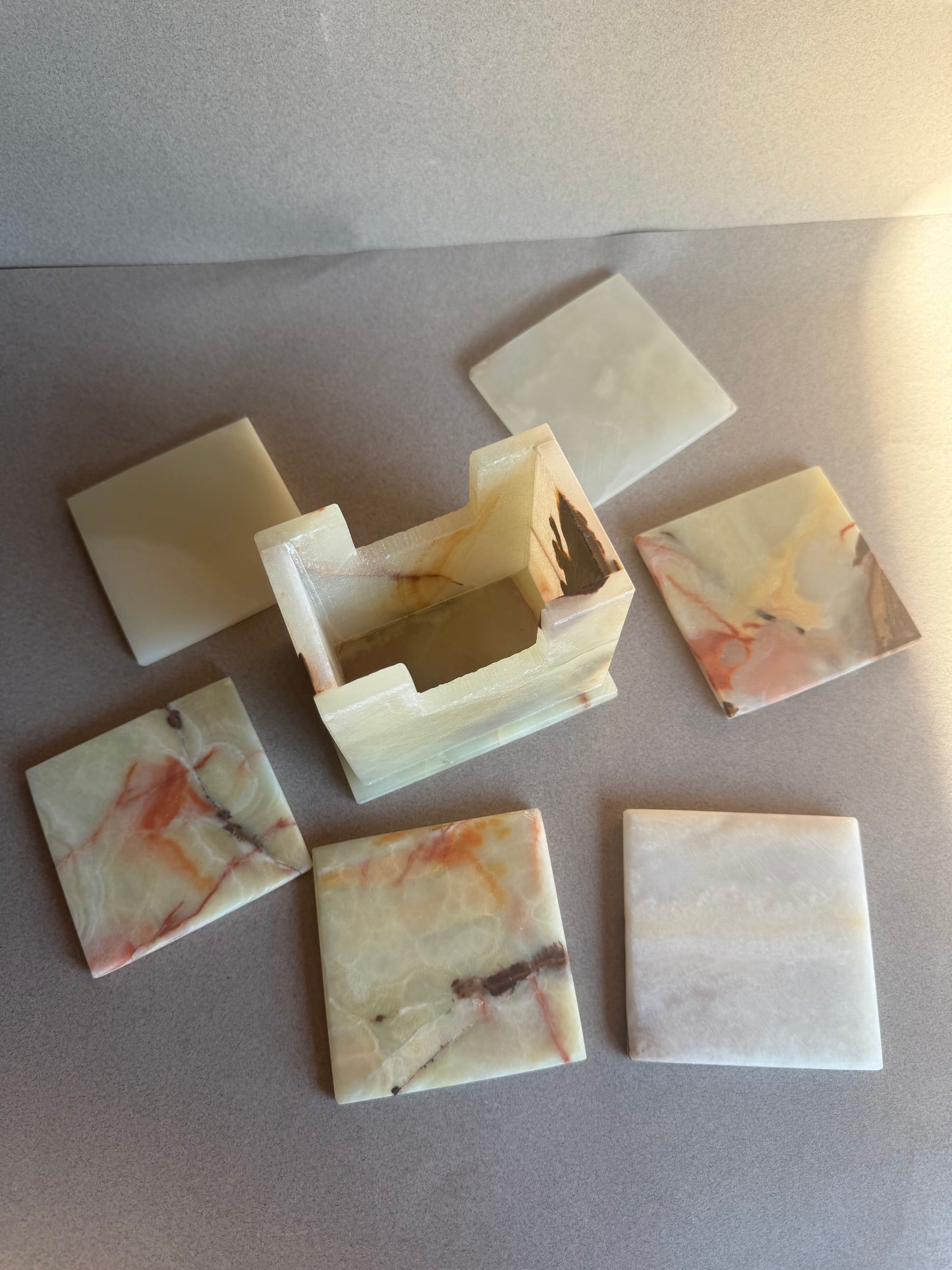 Onyx coaster holder in ivory and beige stone with natural amber and rust veining, square shape with open slot.