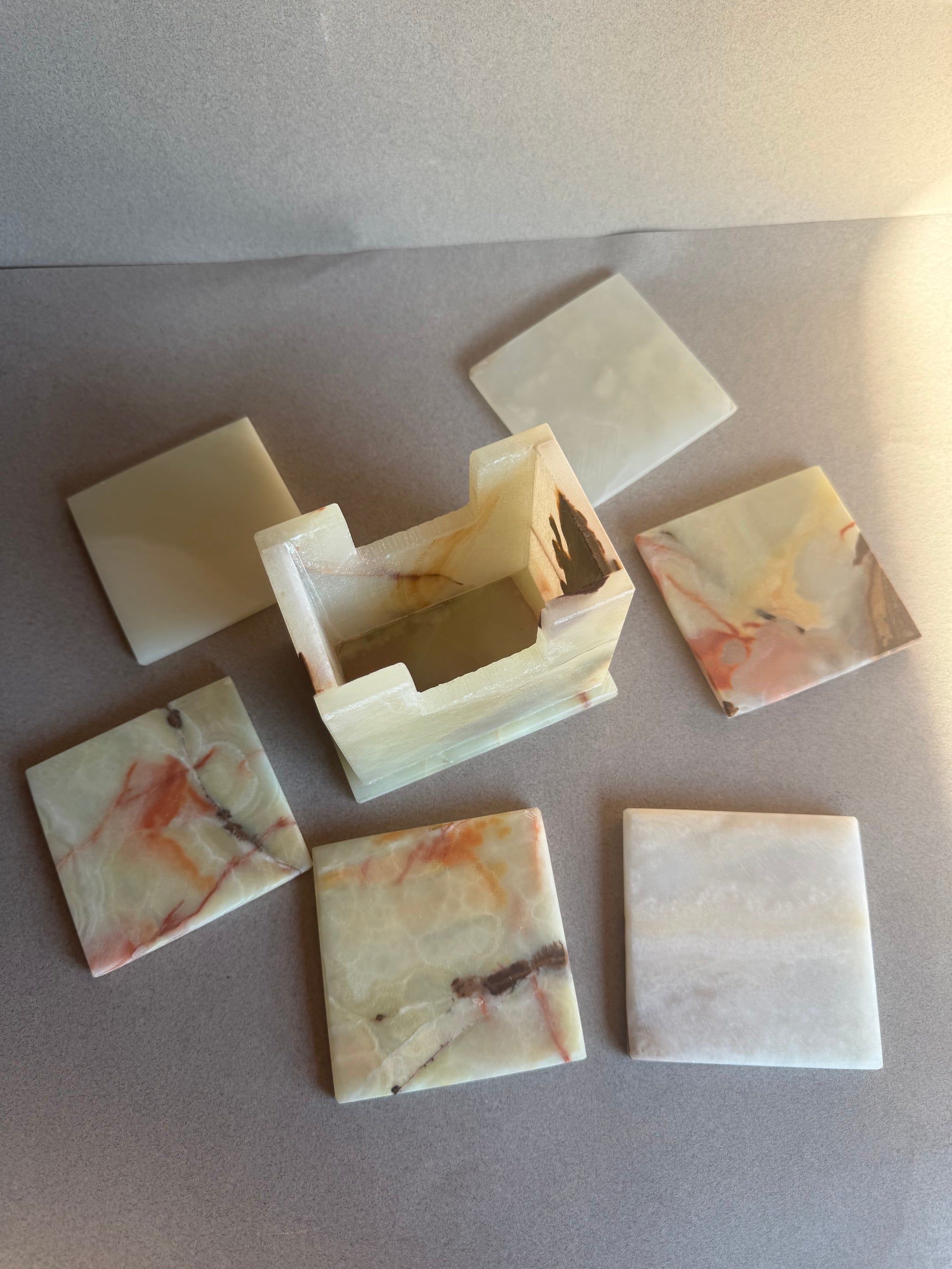 Onyx coaster holder in ivory and beige stone with natural amber and rust veining, square shape with open slot.