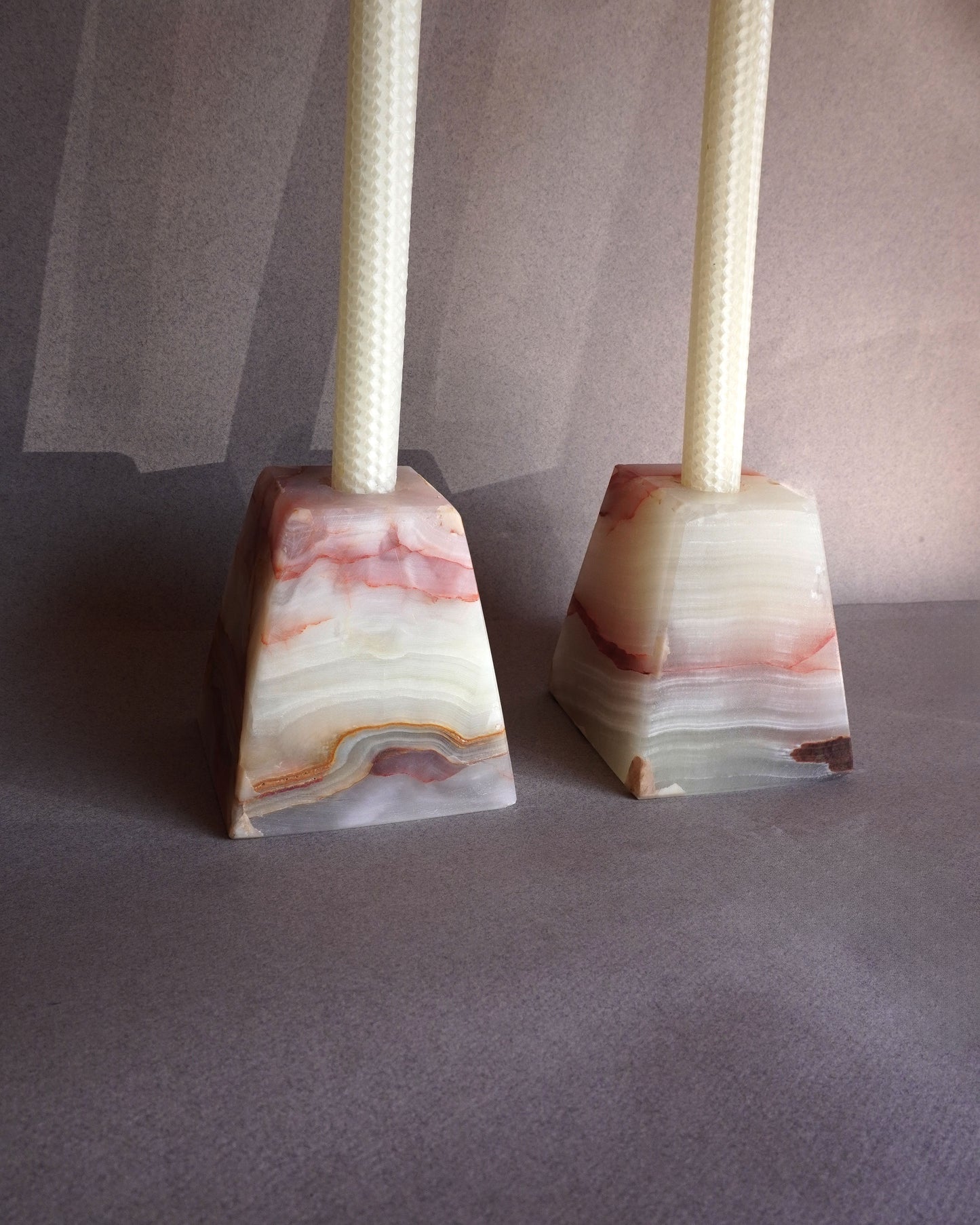 Two marble stone onyx candle holders with woven candlesticks on a gray surface.