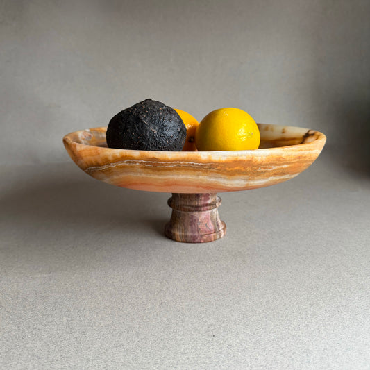 Hand carved onyx pedestal bowl with amber, rust, and ivory veining styled with citrus
