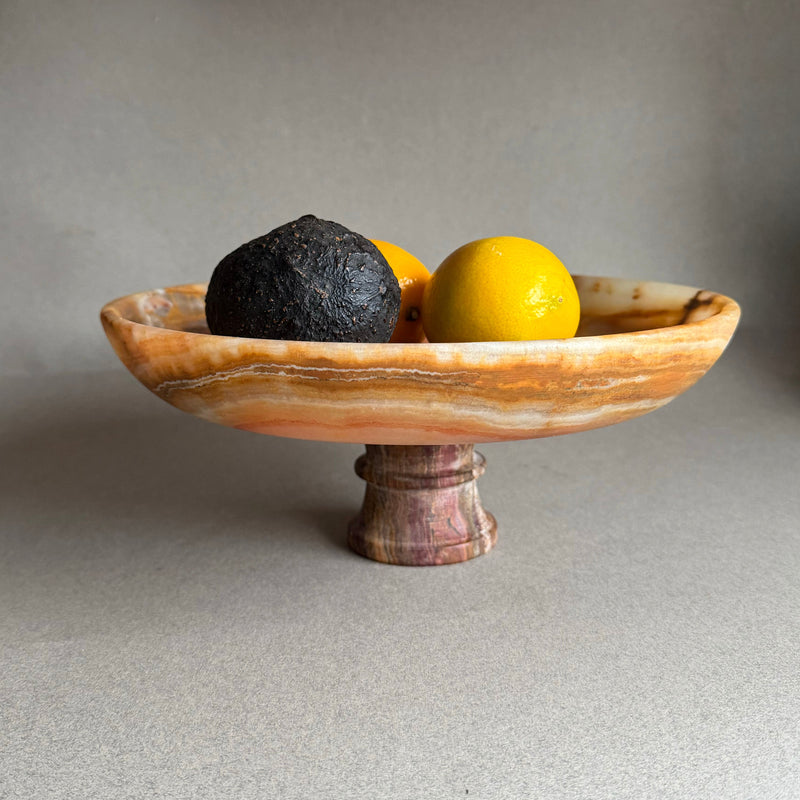 Hand carved onyx pedestal bowl with amber, rust, and ivory veining styled with citrus
