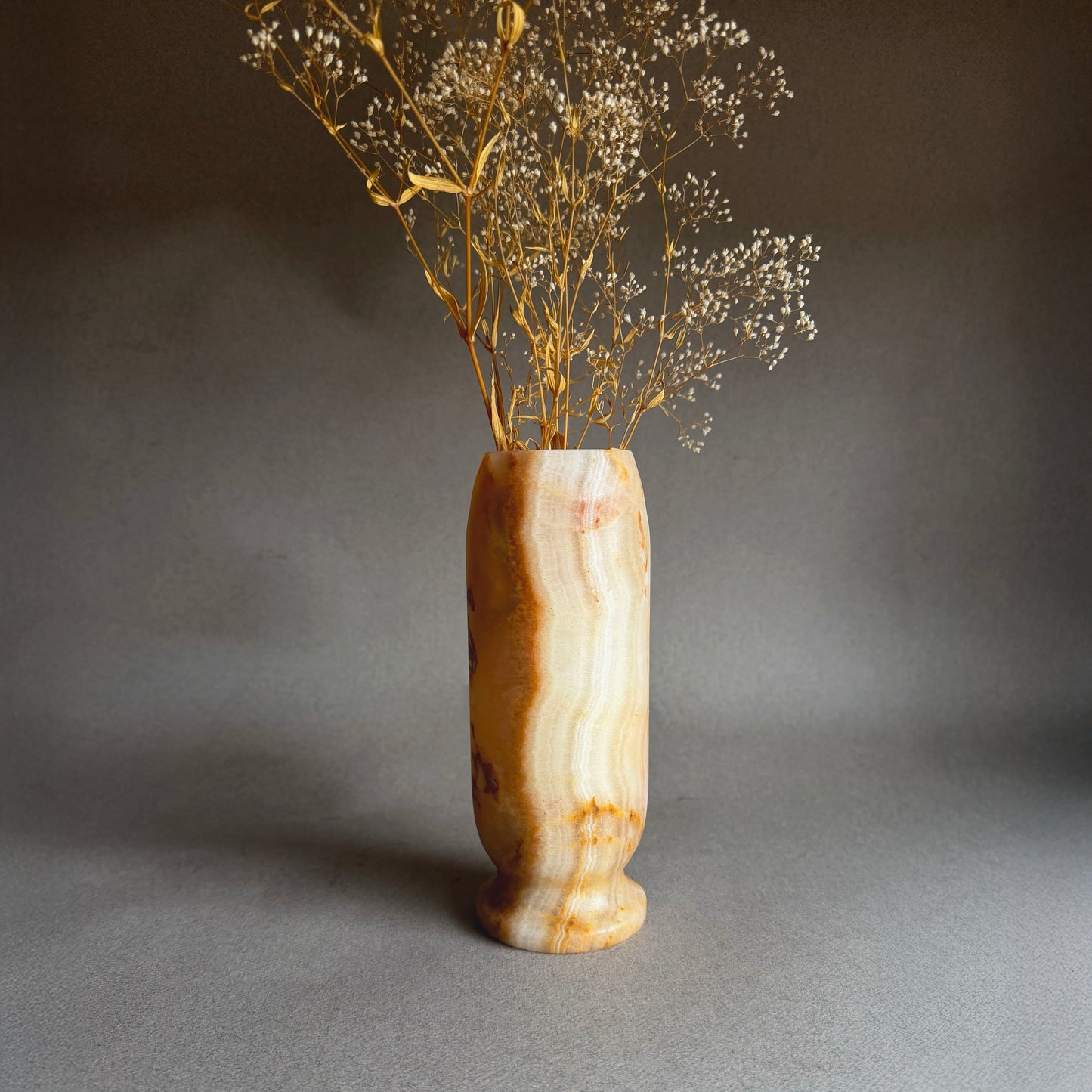 Decorative peach white orange honey onyx vase with dried flowers on a gray background