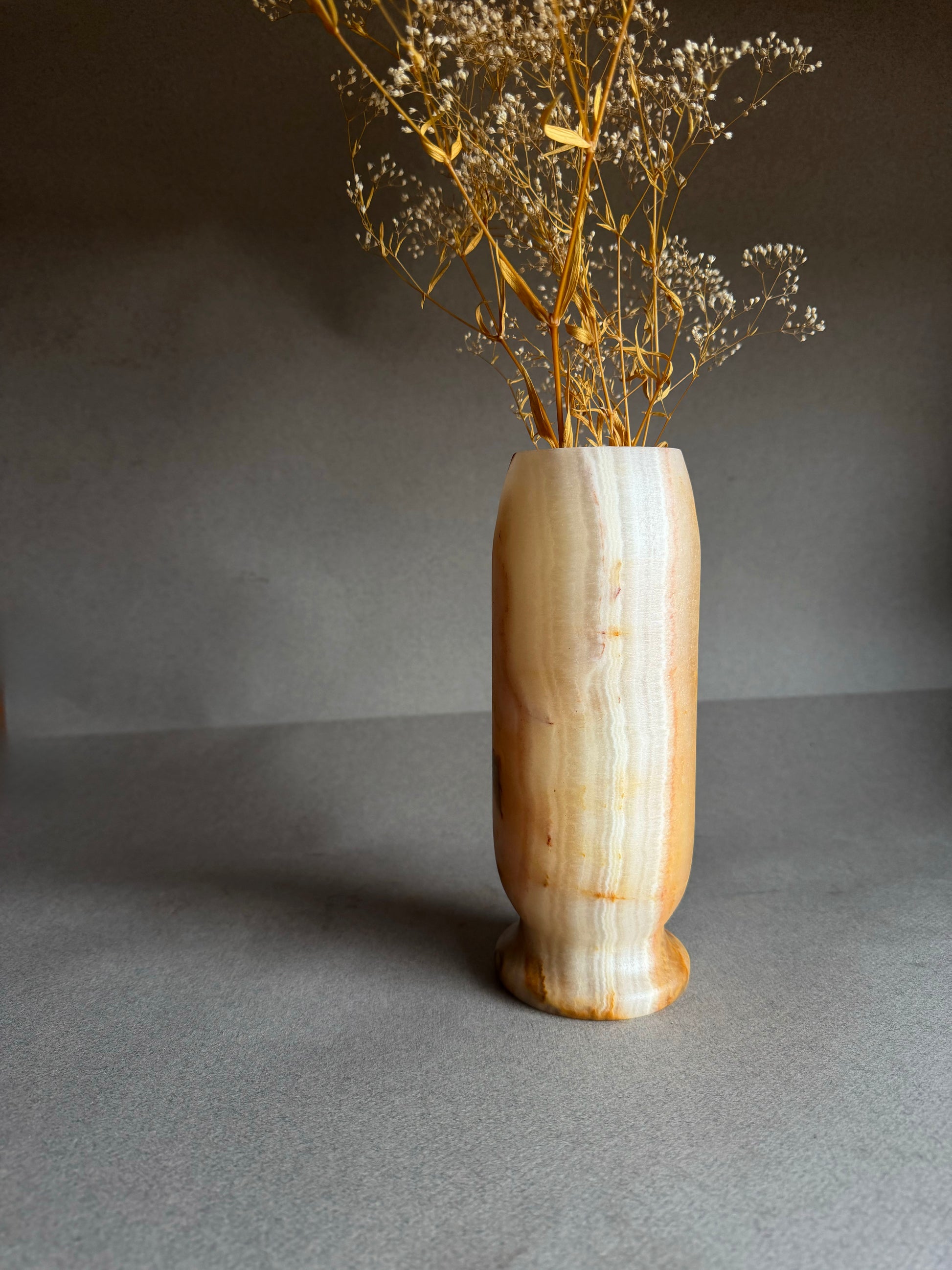 peach white orange honey stone marble onyx vase with dried flowers on a gray background
