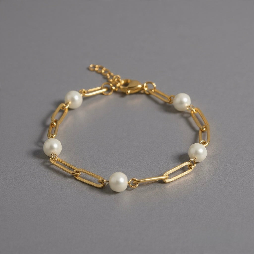 Product photo of gold waterproof paperclip bracelet with pearls and extender chain on gray surface.
