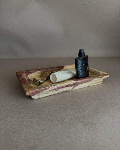 Hand-carved purple and chestnut onyx tray with ivory, green, and amber veining, styled as a vanity catchall
