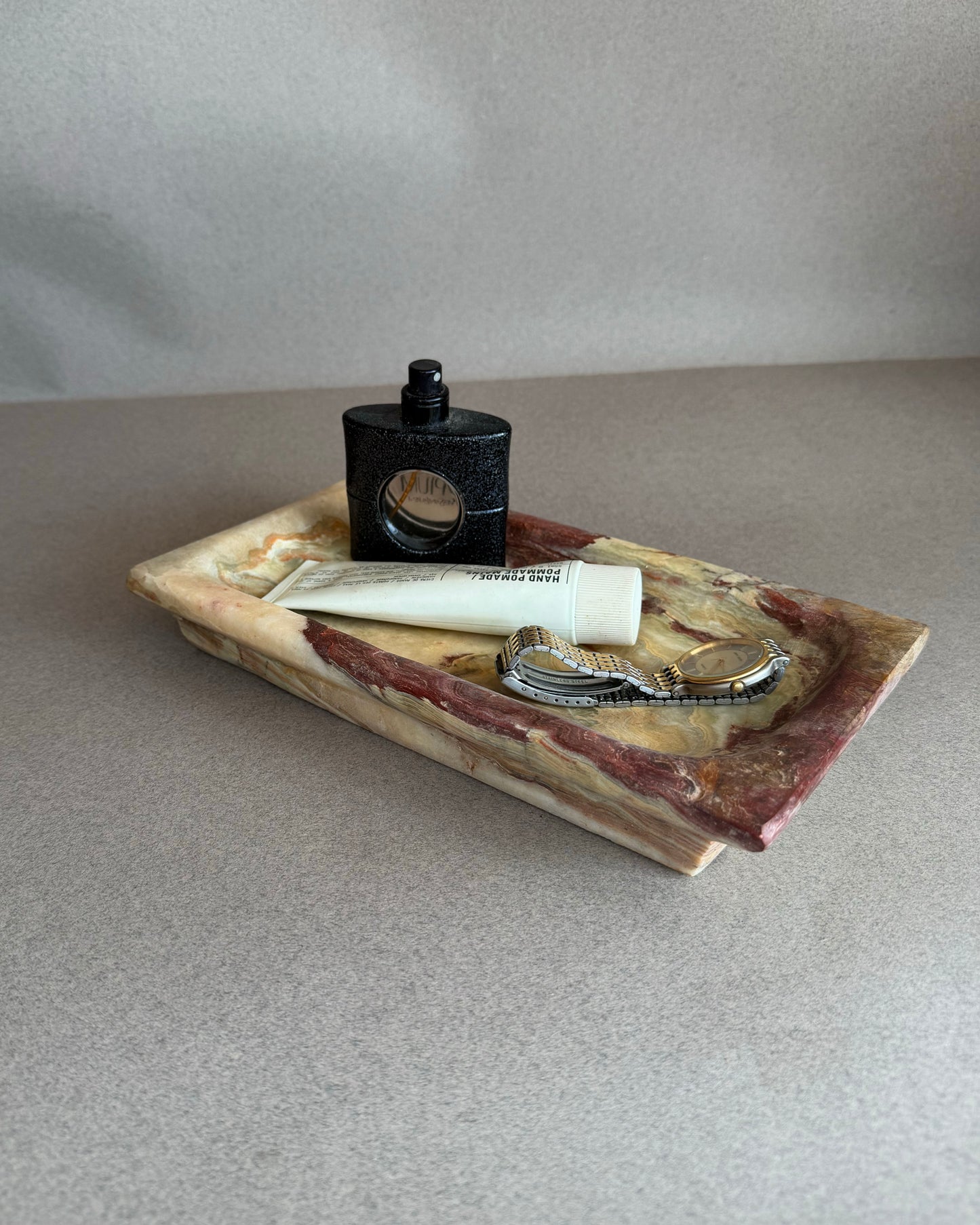 Hand-carved purple and chestnut onyx tray with ivory, green, and amber veining, styled as a vanity catchall
