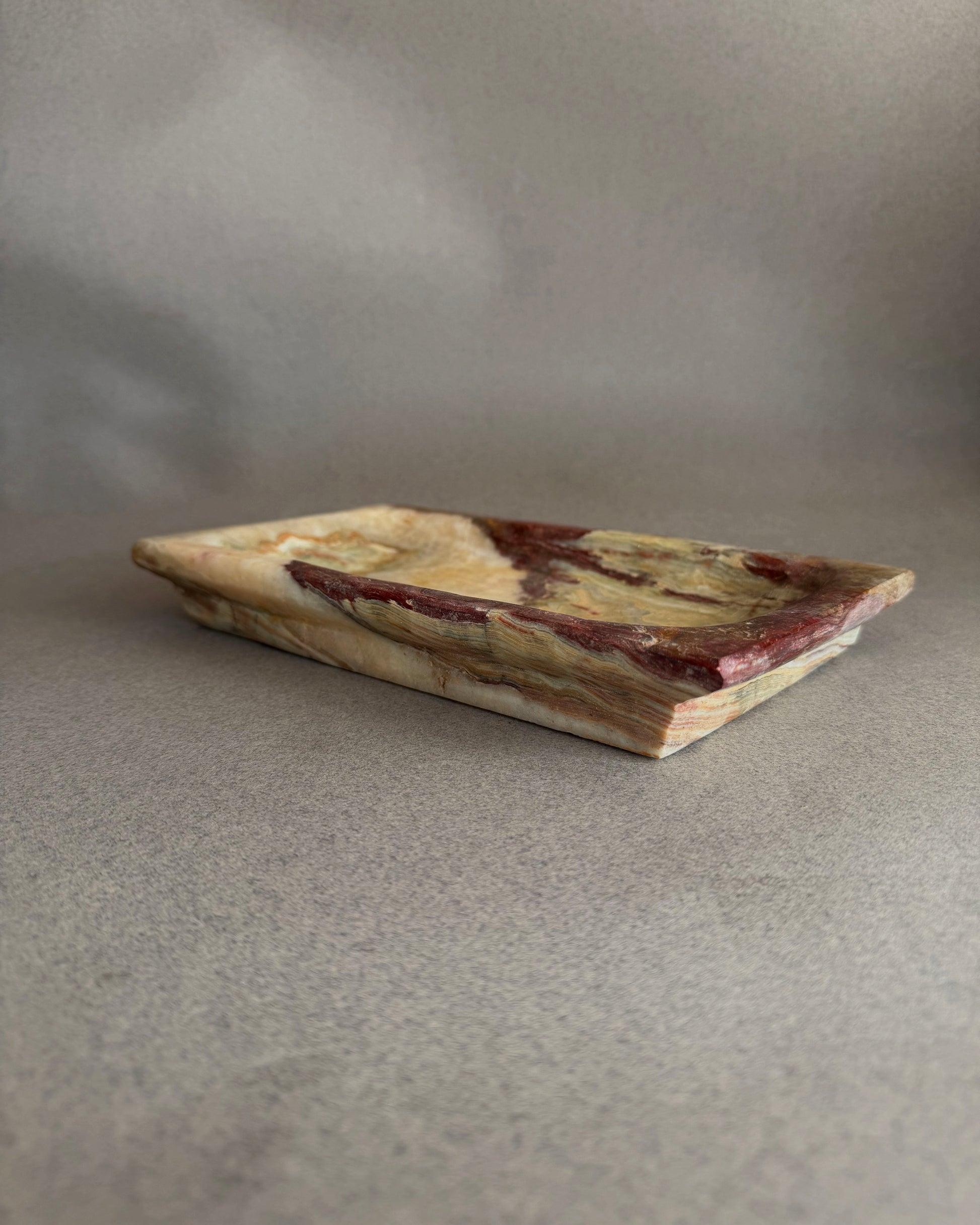 Stone catchall tray carved from solid onyx with painterly purple, chestnut, and moss green mineral patterns
