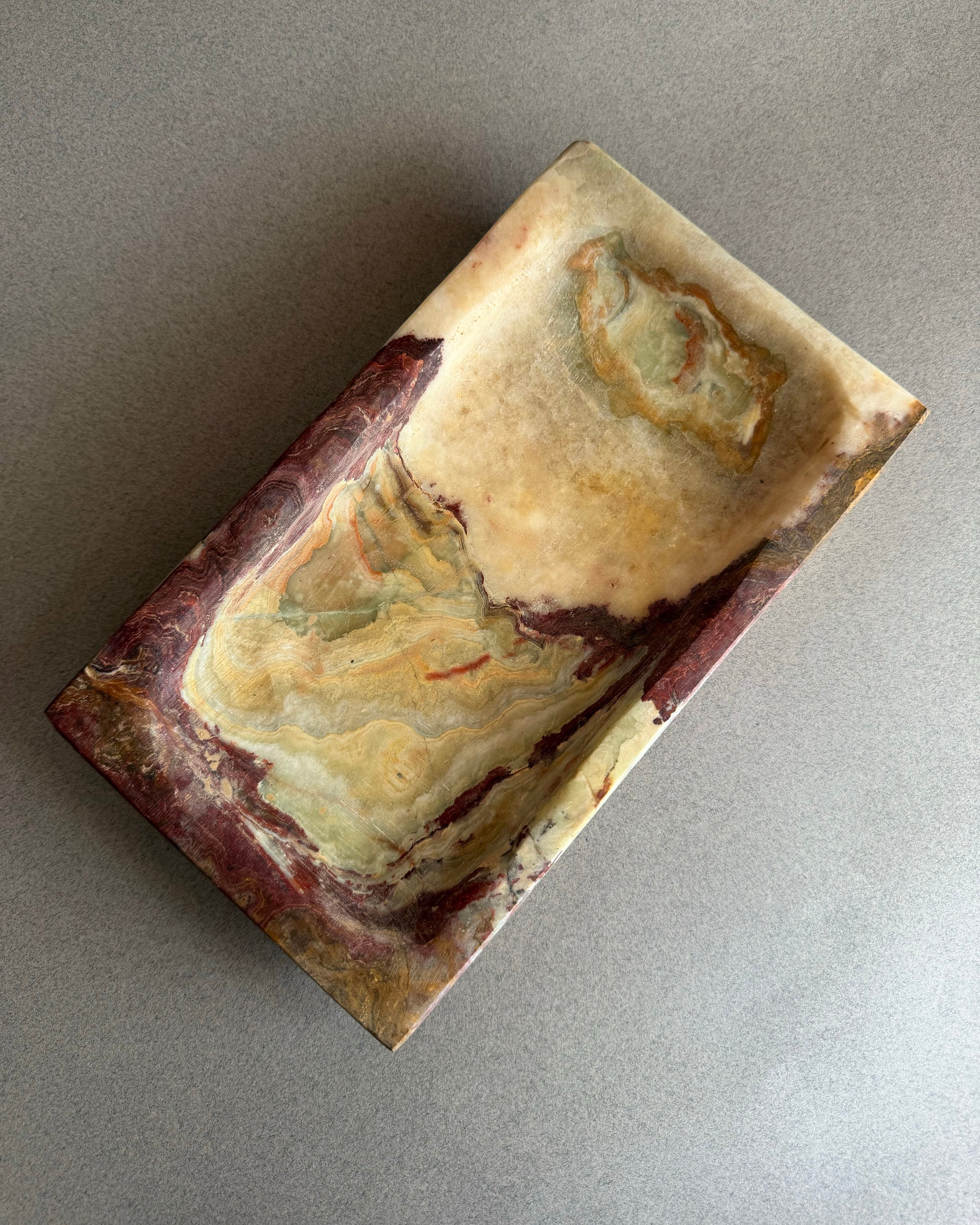 Stone catchall tray carved from solid onyx with painterly purple, chestnut, and moss green mineral patterns
