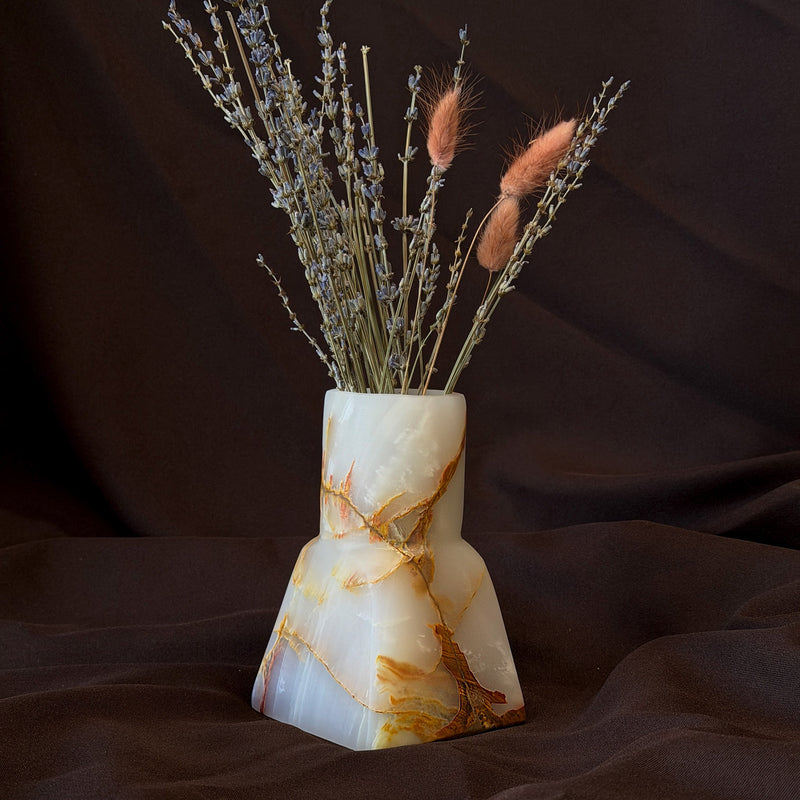 Stepped onyx bud vase in milk white with amber and rust veins, holding dried lavender and pink bunny tail grass against dark brown fabric