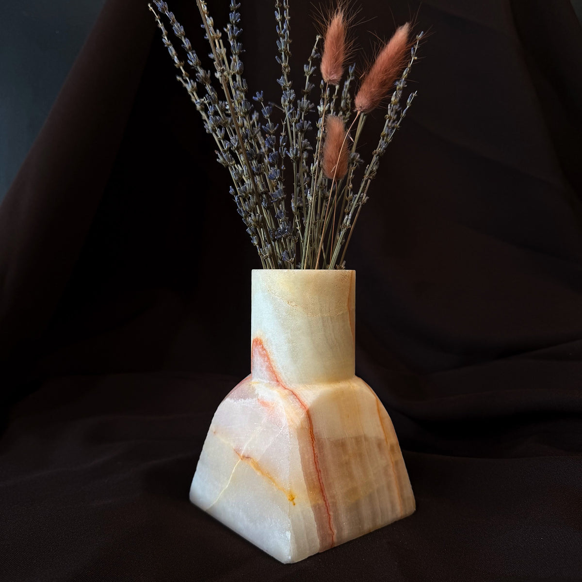 Stepped onyx dune vase in milk white with a coral seam down one face, holding dried lavender and pink bunny tail grass against dark fabric