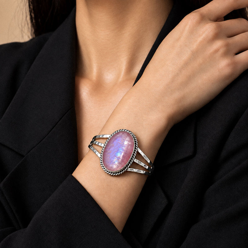 Pink moonstone silver cuff bracelet worn on the wrist against a black blazer sleeve.