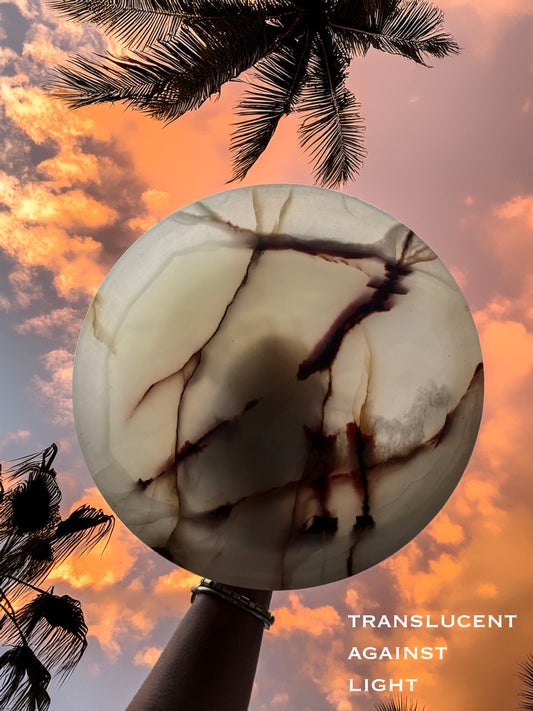 Translucent pink onyx stone held against a sunset sky with palm trees
