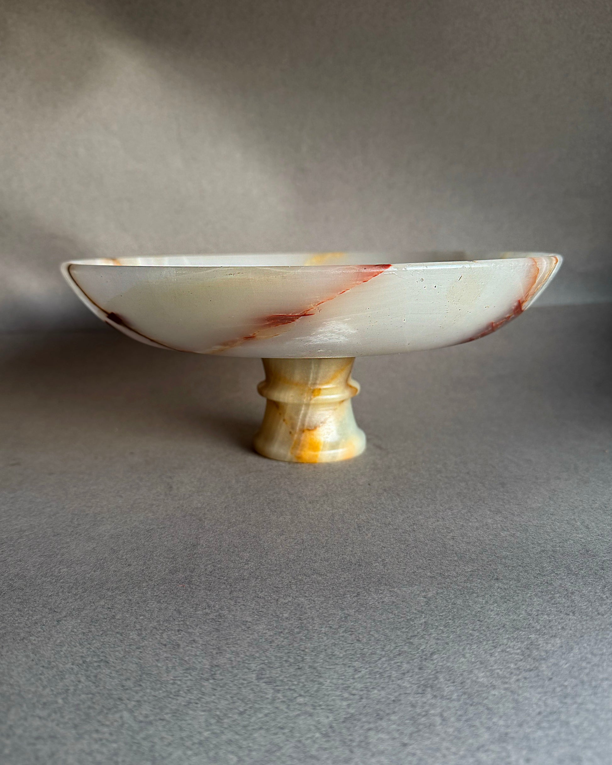 Decorative white pink onyx dish with brown and yellow speckles on a gray background