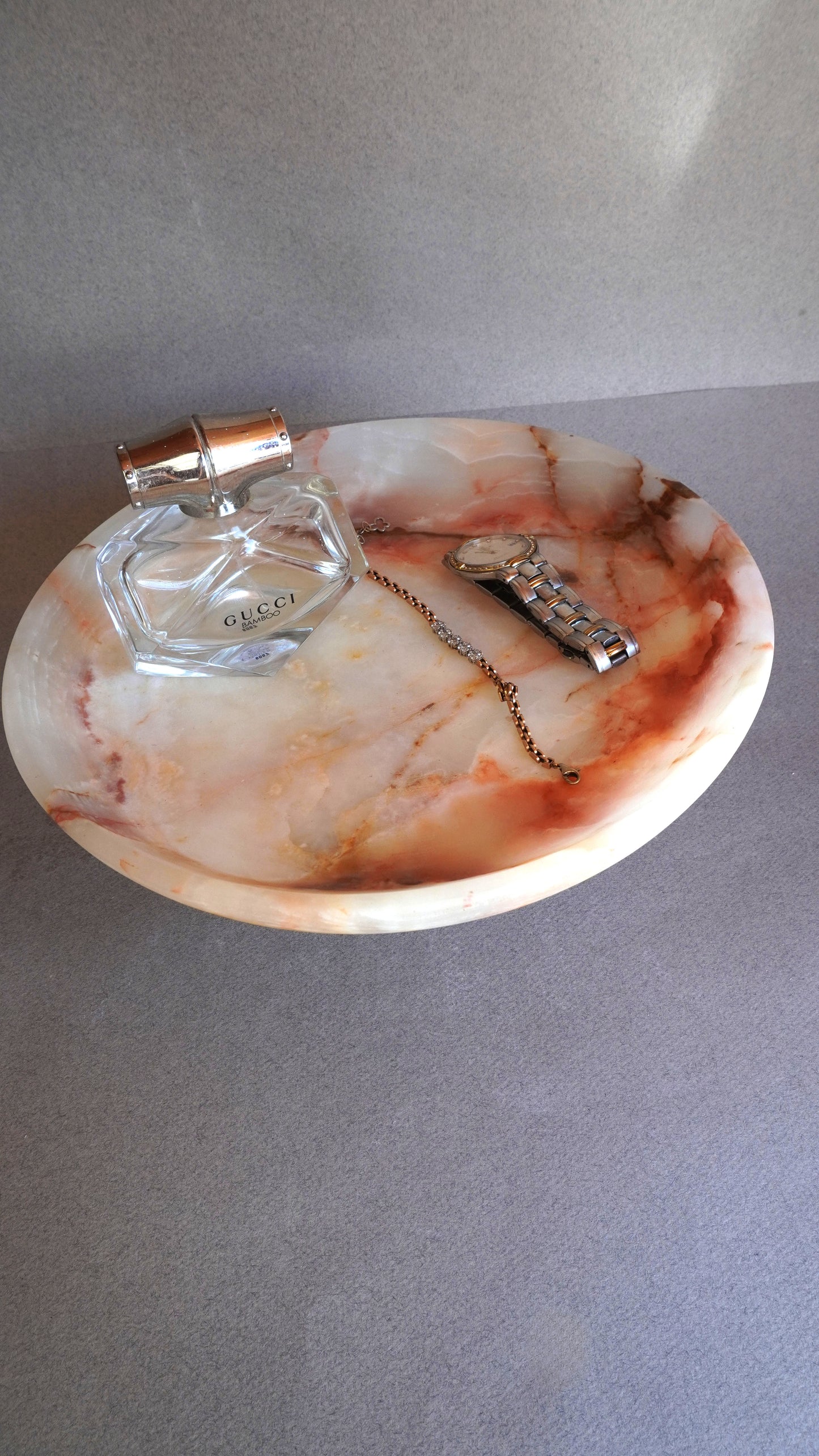 pink onyx  Decorative stone dish with a perfume bottle and necklace on a gray surface