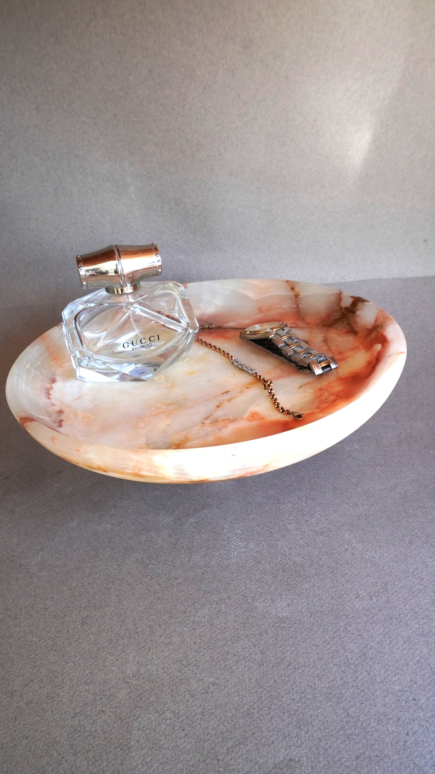 pink onyx  Onyx stone tray with a perfume bottle and jewelry on a gray surface