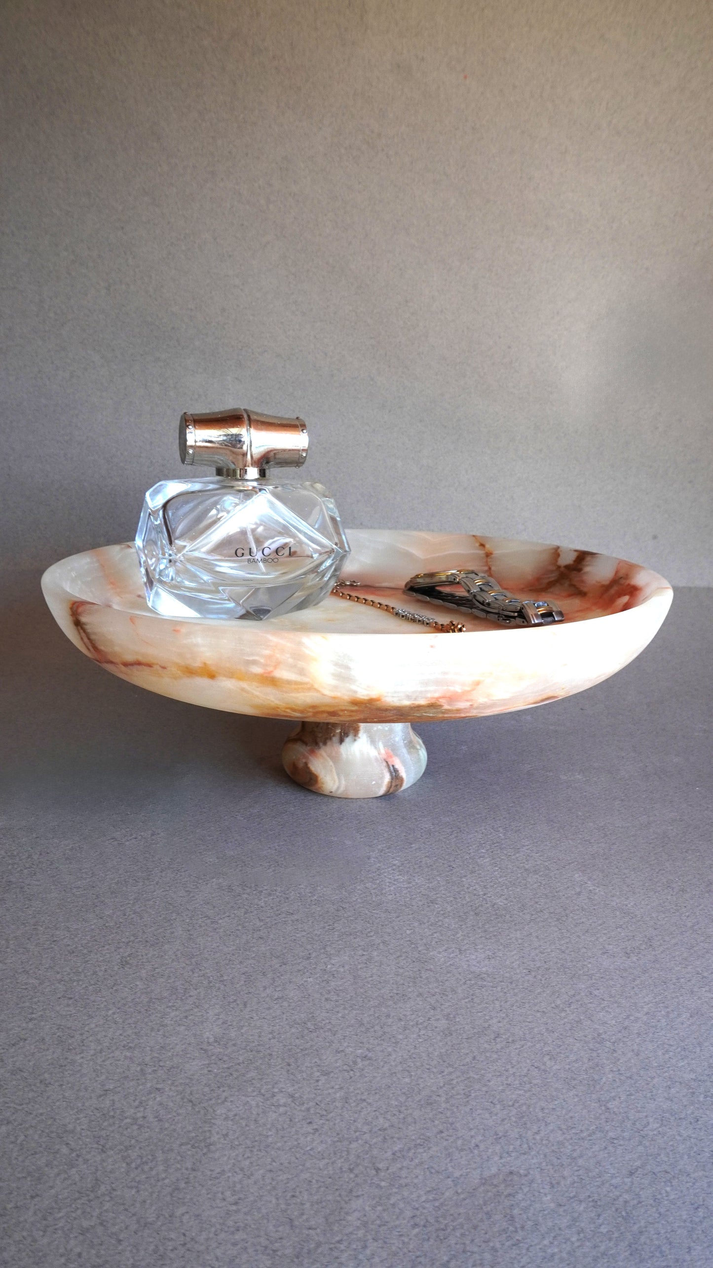 pink onyx  Decorative glass bottle on a pedestal bowl against a plain background