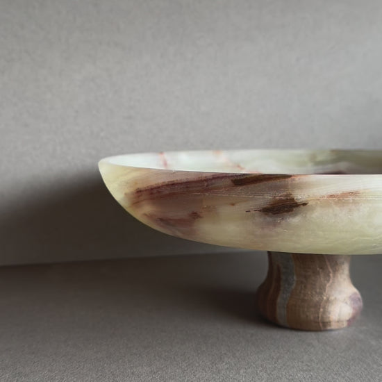 Hand-carved onyx pedestal bowl with cream, rust, and amber veining, displayed on a neutral tabletop

