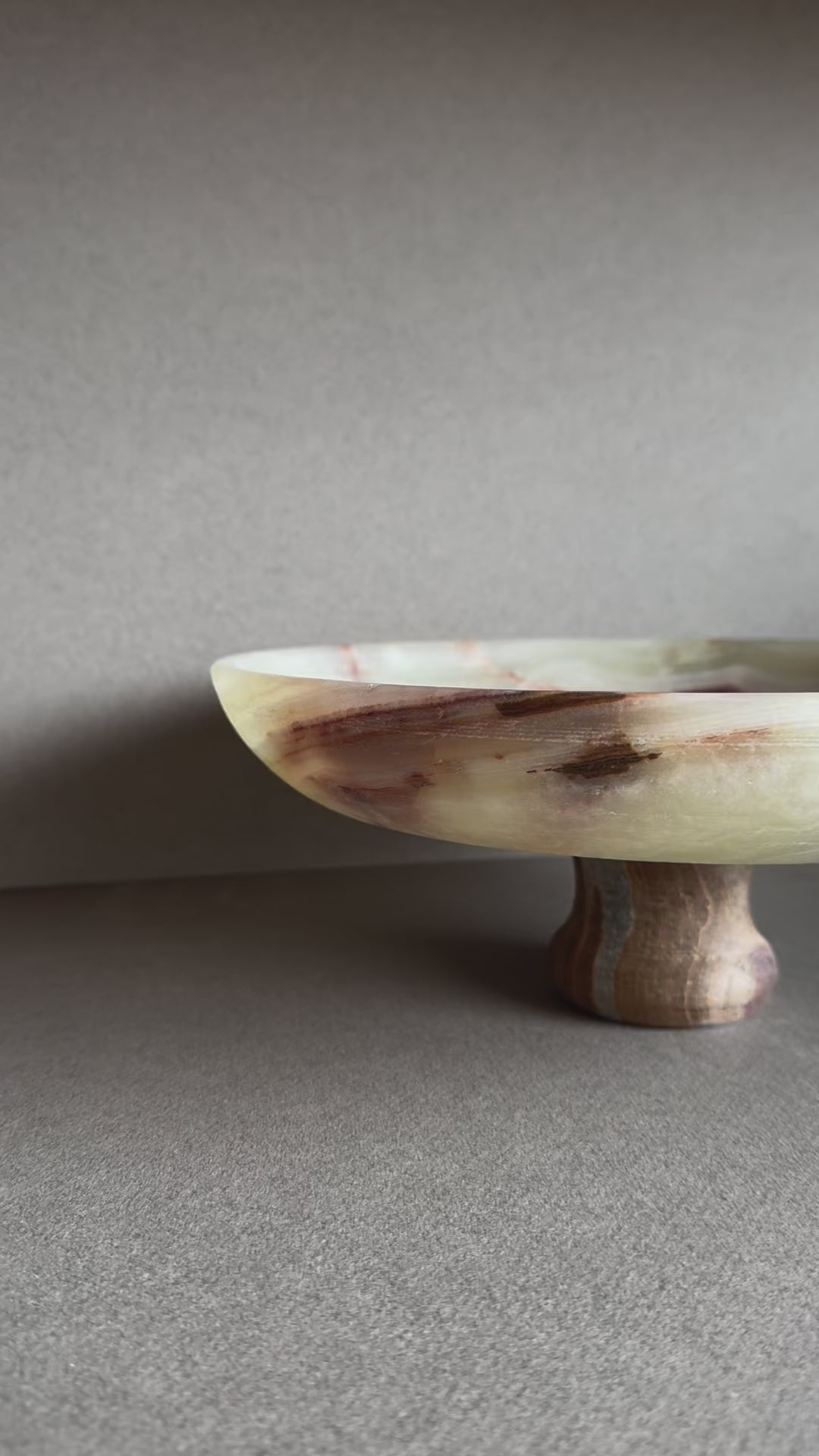 Hand-carved onyx pedestal bowl with cream, rust, and amber veining, displayed on a neutral tabletop

