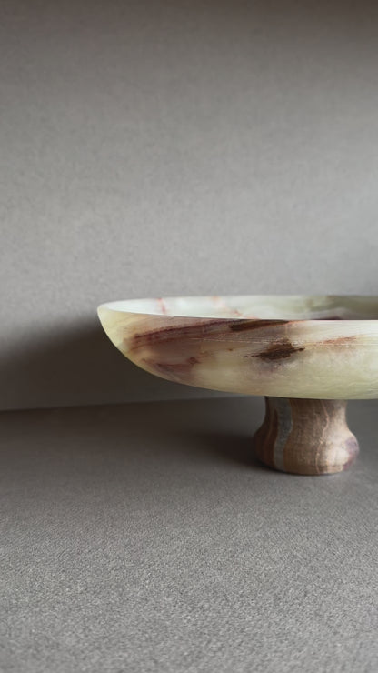 Hand-carved onyx pedestal bowl with cream, rust, and amber veining, displayed on a neutral tabletop

