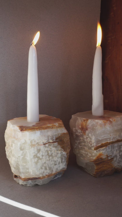 Pair of sculptural onyx candle holders with milky ivory stone and warm caramel veining photographed in natural light
