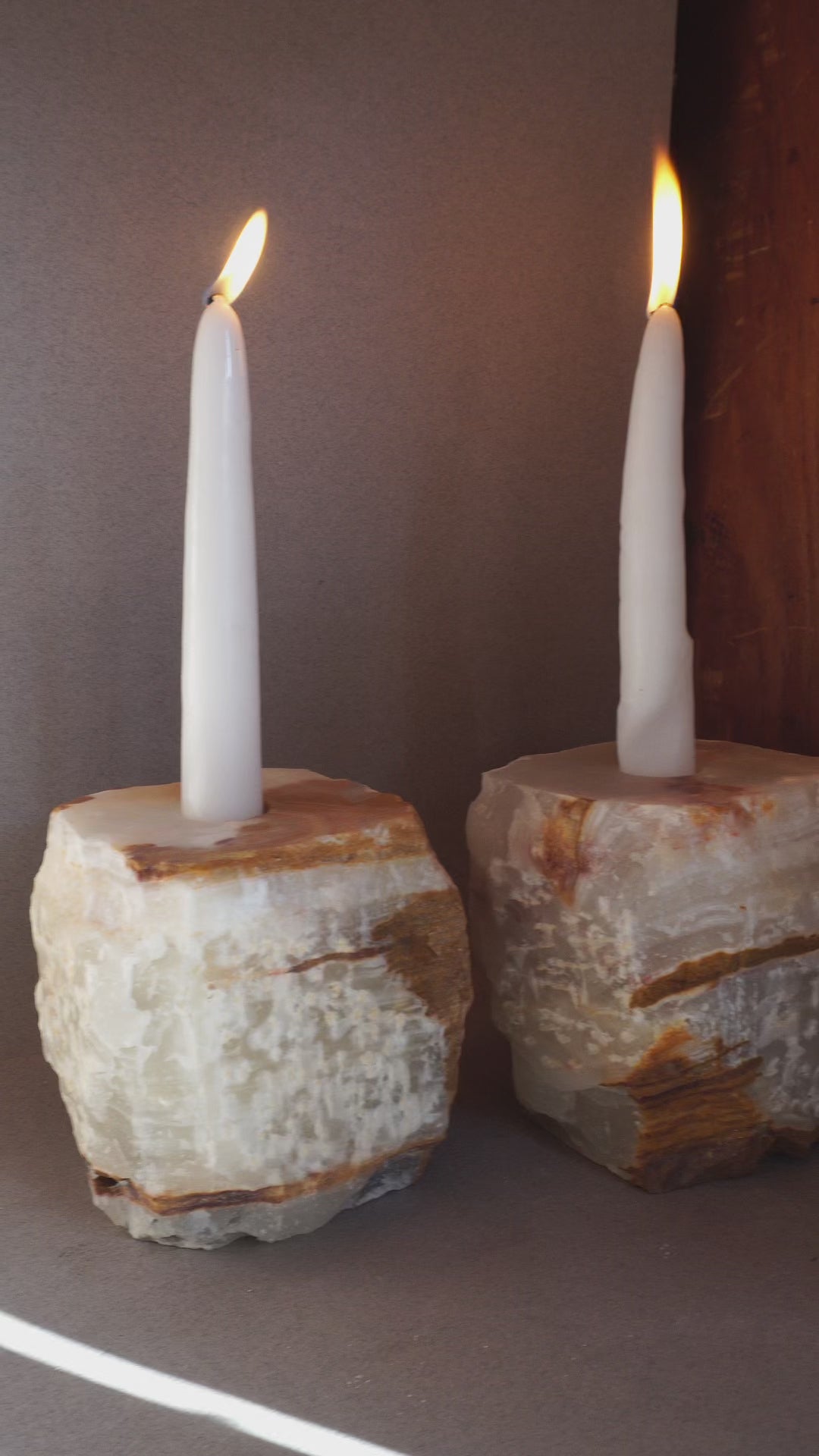 Pair of sculptural onyx candle holders with milky ivory stone and warm caramel veining photographed in natural light
