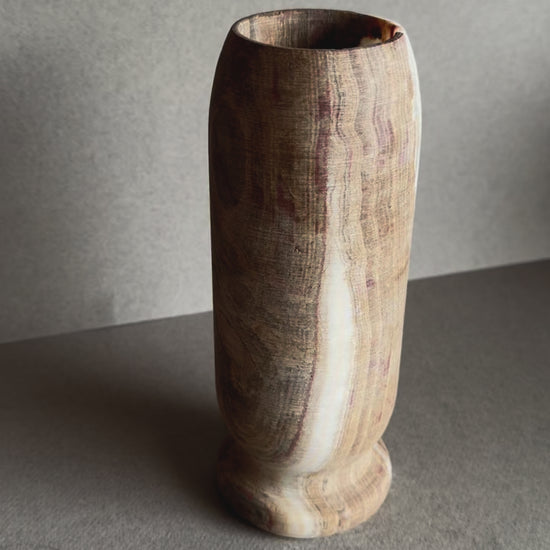 Tall onyx vase with dramatic rose-toned mineral bloom, hand-carved with a pedestal base and natural matte finish.

