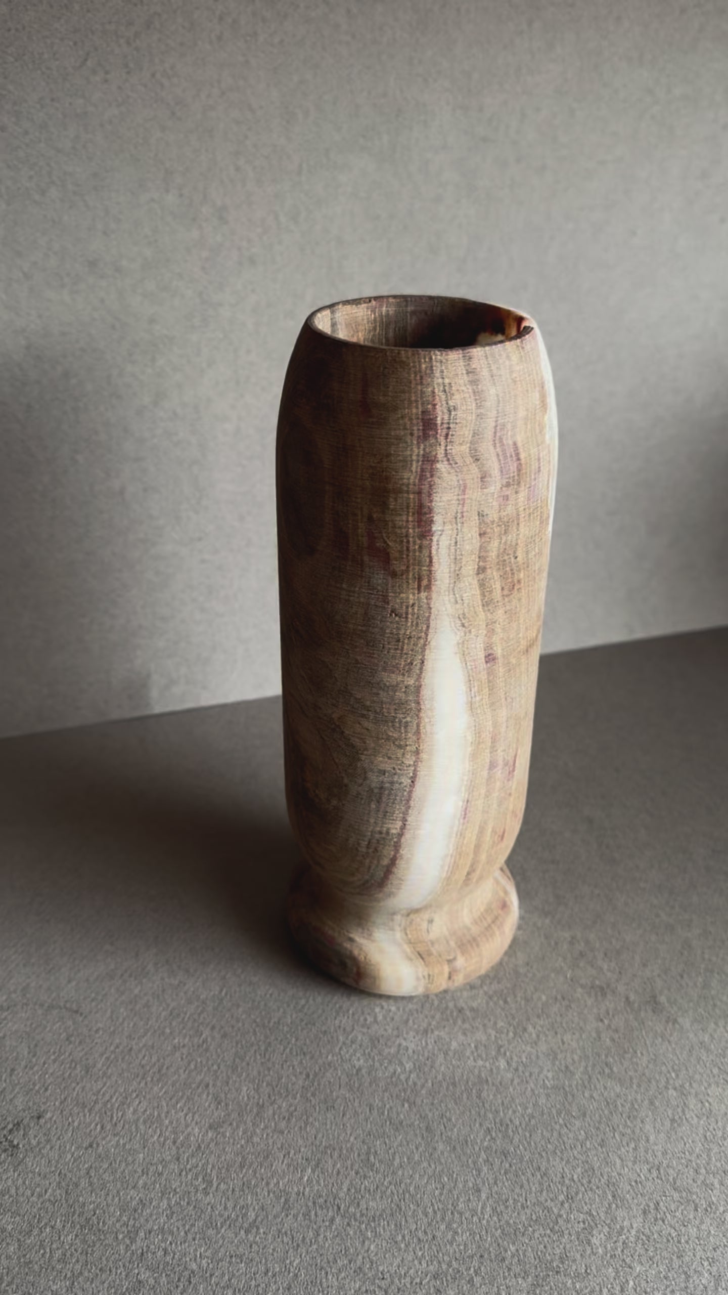 Tall onyx vase with dramatic rose-toned mineral bloom, hand-carved with a pedestal base and natural matte finish.


