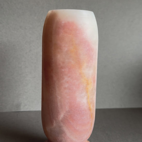 Front view of tall stone vase with layered pink, orange, and tan hues.

