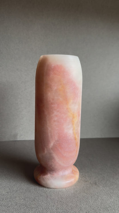 Front view of tall stone vase with layered pink, orange, and tan hues.

