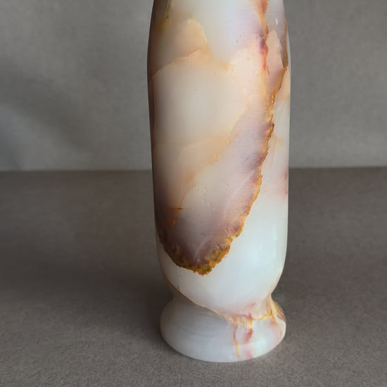 Natural onyx flower vase with soft pink, ivory, and caramel veining, minimalist stone decor photographed on neutral background
