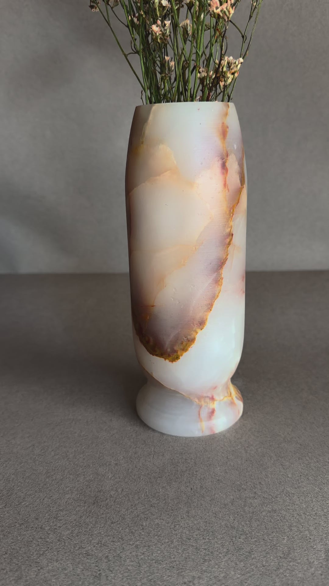 Natural onyx flower vase with soft pink, ivory, and caramel veining, minimalist stone decor photographed on neutral background
