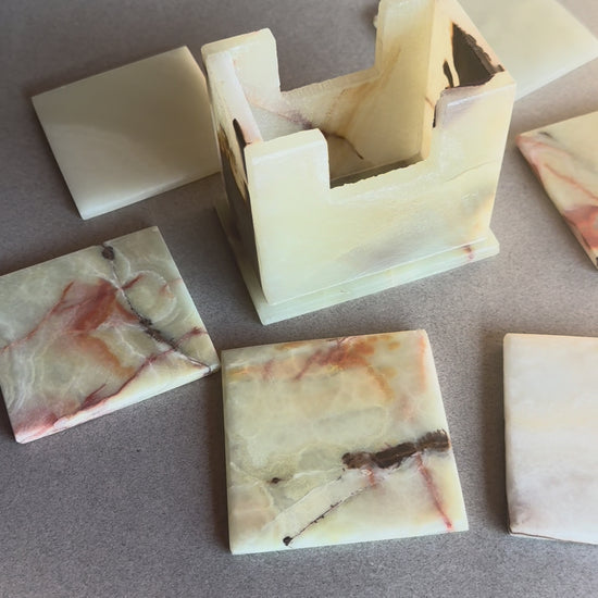 Onyx coaster set with six square stone coasters and a matching holder, ivory and amber colors with natural veining.