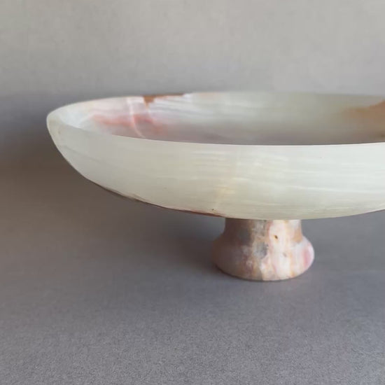 Cream and sage onyx bowl with pedestal base, partially lit to highlight stone’s translucency.