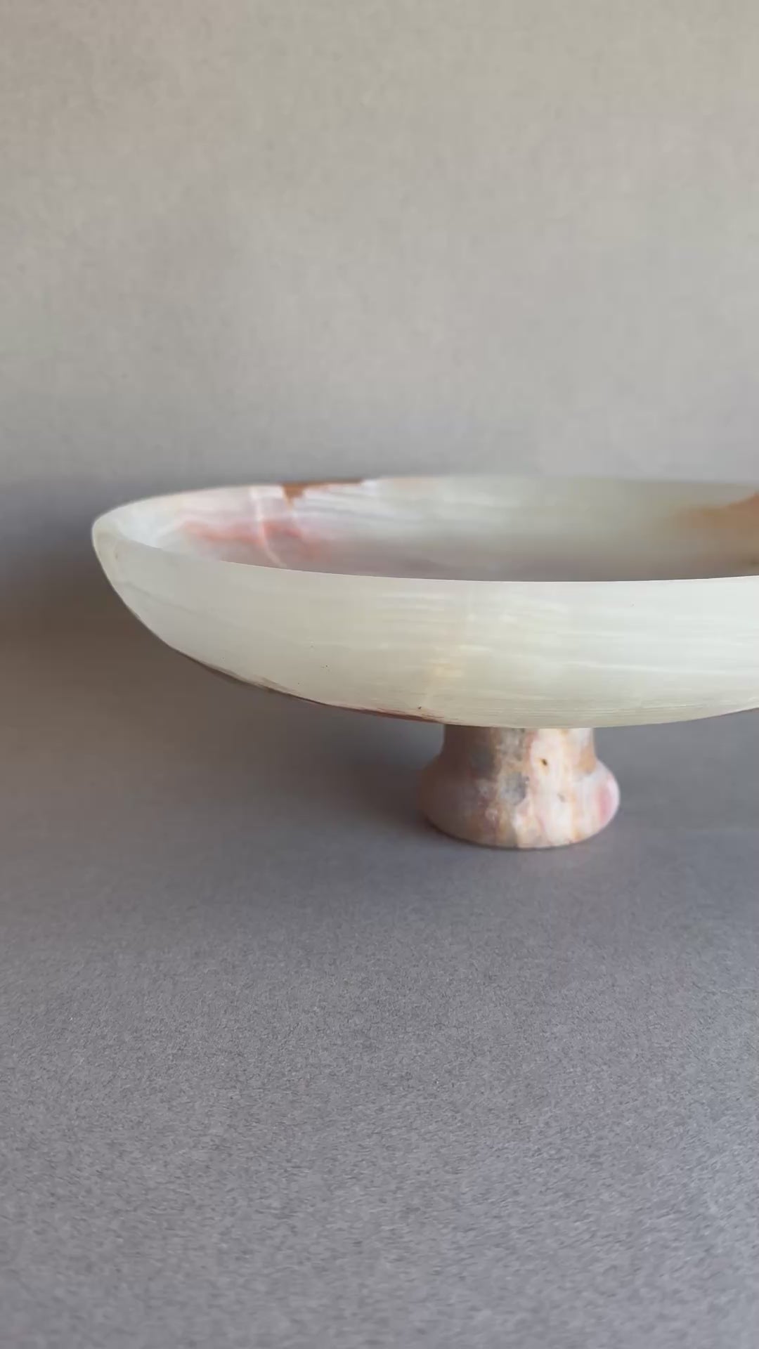 Cream and sage onyx bowl with pedestal base, partially lit to highlight stone’s translucency.