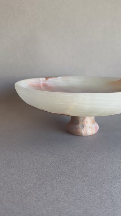 Cream and sage onyx bowl with pedestal base, partially lit to highlight stone’s translucency.