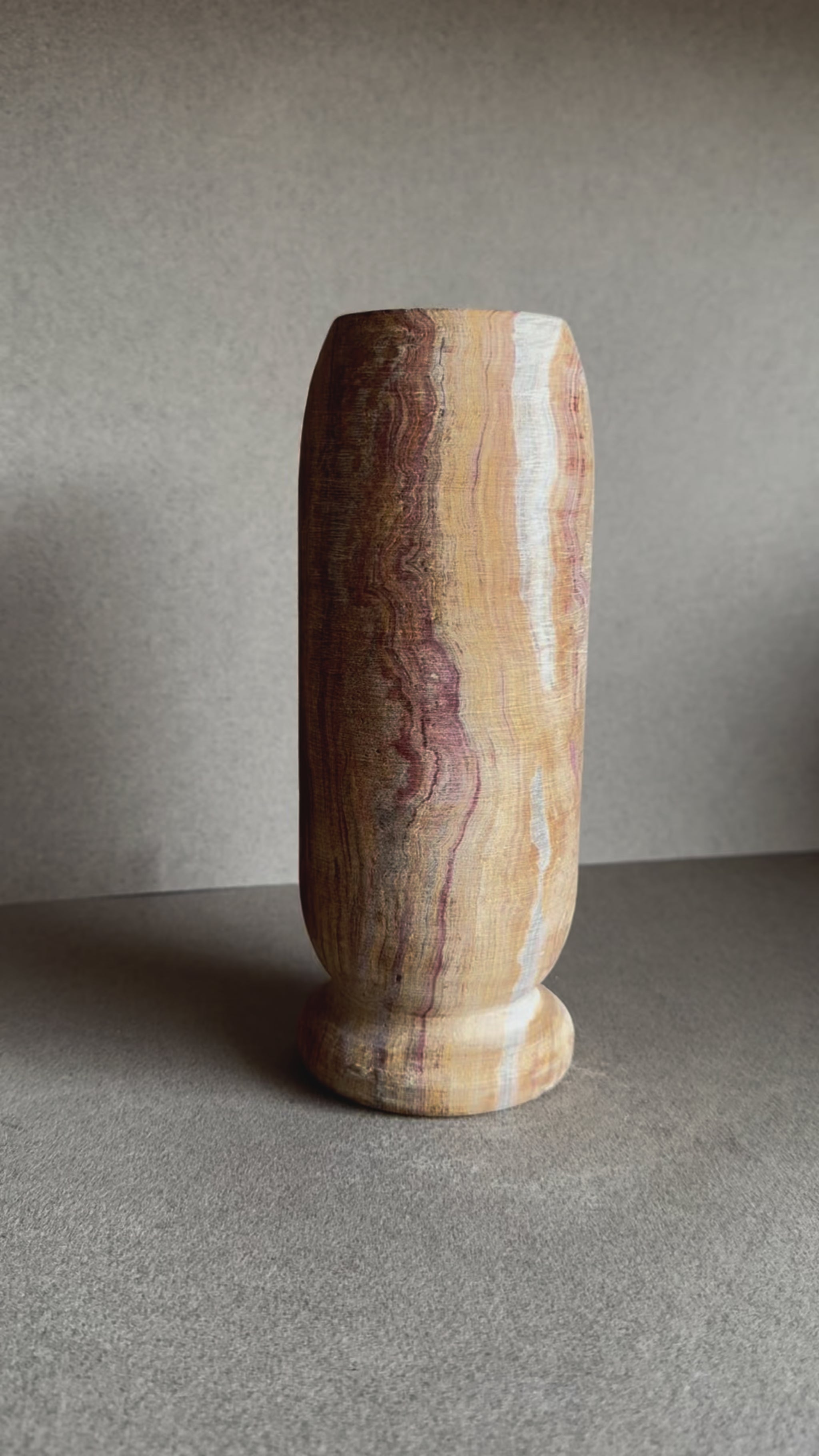 Onyx vase in layered sandstone and rose tones with smooth matte finish and cylindrical shape.

