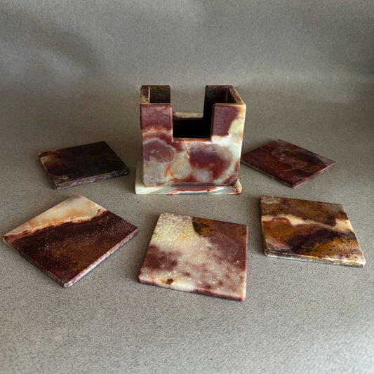 Marble-patterned coasters with a holder on a gray surface plum onyx coaster with warm rust and amber mineral bands resting on minimal neutral background
