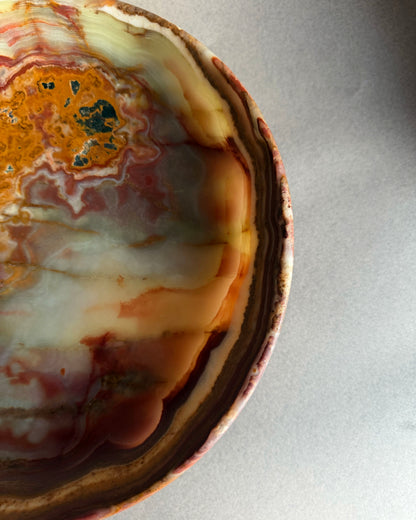 Raw onyx pedestal bowl carved from a single block of stone featuring organic veining in green, orange, plum, and cream tones
