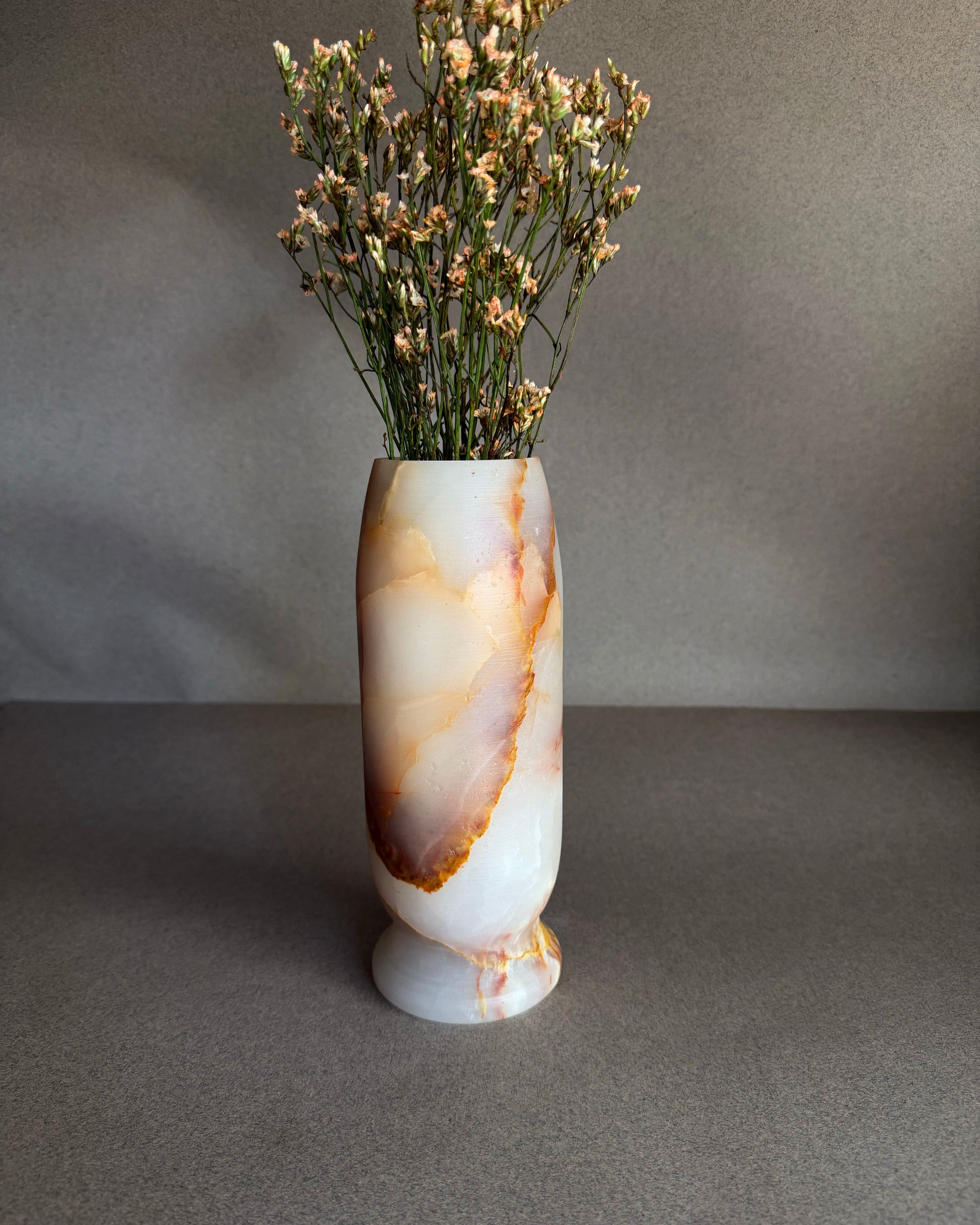 Decorative vase with a natural stone pattern containing dried flowers on a gray background