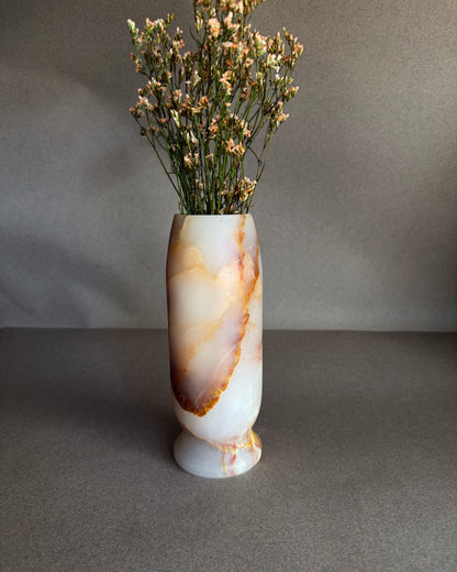 Decorative vase with a natural stone pattern containing dried flowers on a gray background
