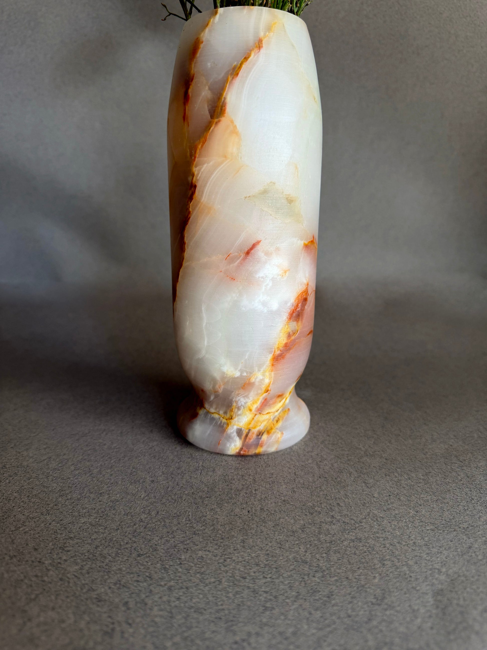 Sculptural pedestal vase carved from solid onyx stone featuring translucent white, blush pink, and amber mineral patterns

