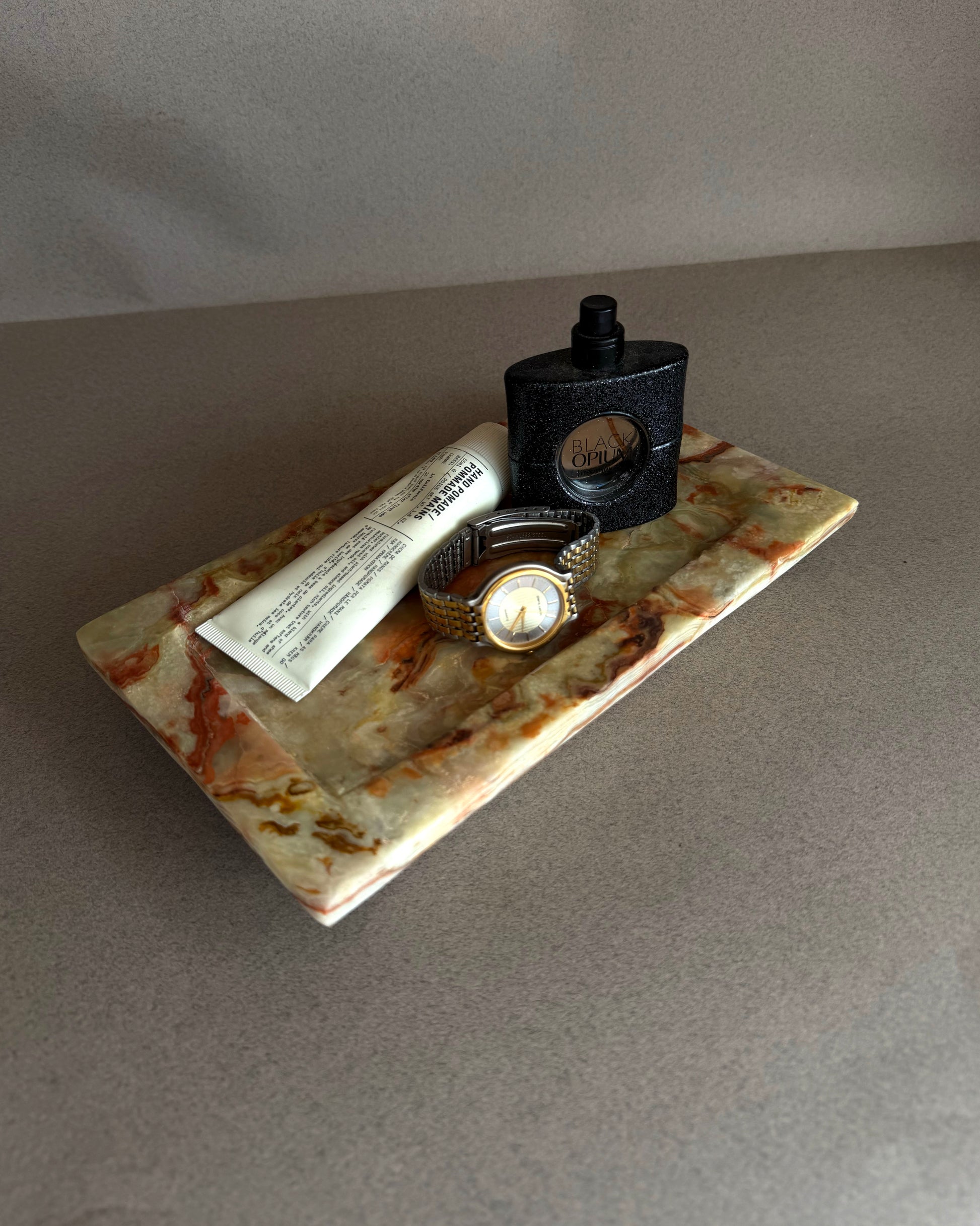 Tray with a watch, tube of cream, and bottle on a gray surface