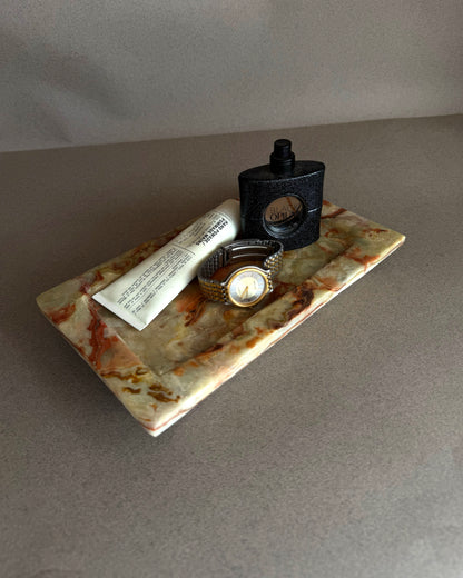 Tray with a watch, tube of cream, and bottle on a gray surface