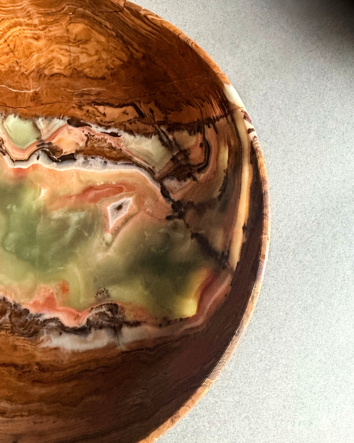Top view of natural onyx pedestal bowl featuring moss green center with swirling red, blush, cream, and brown veining

